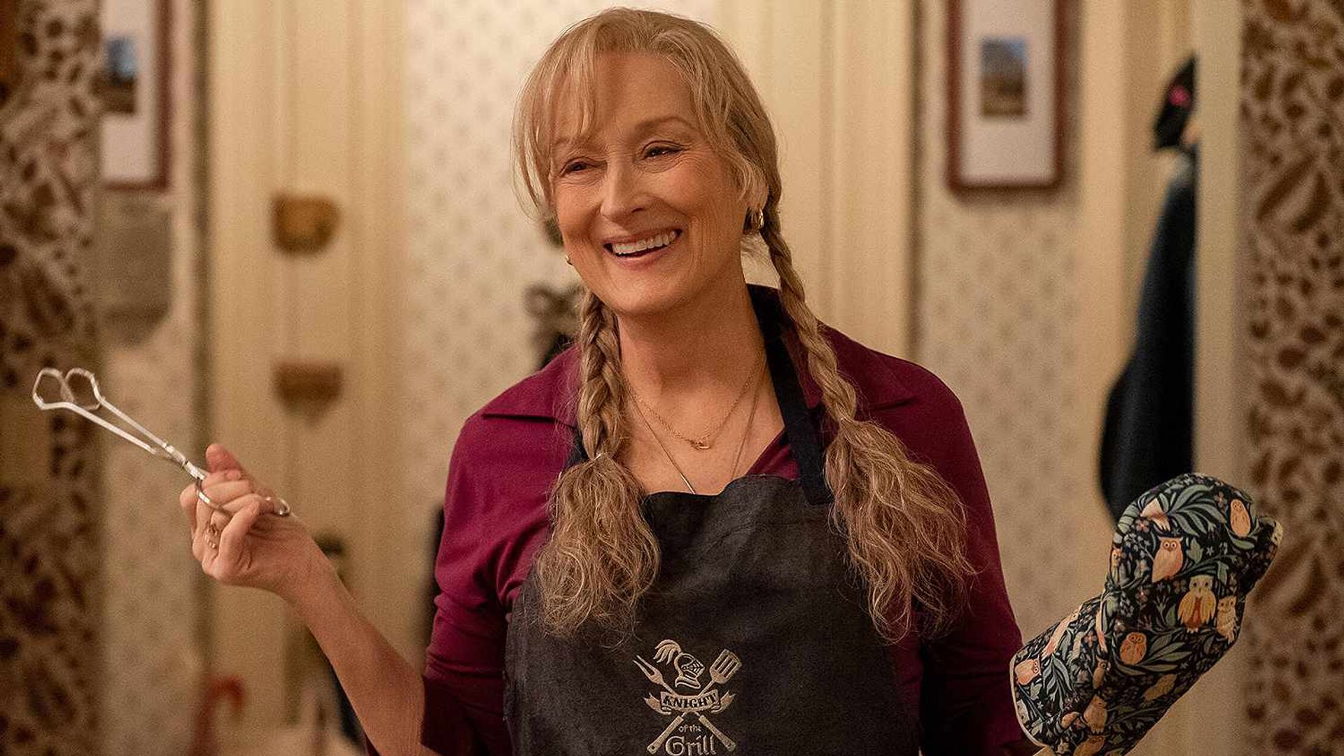 Meryl Streep z warkoczami trzyma szczypce w jednej ręce, mając rękawicę kuchenną na drugiej