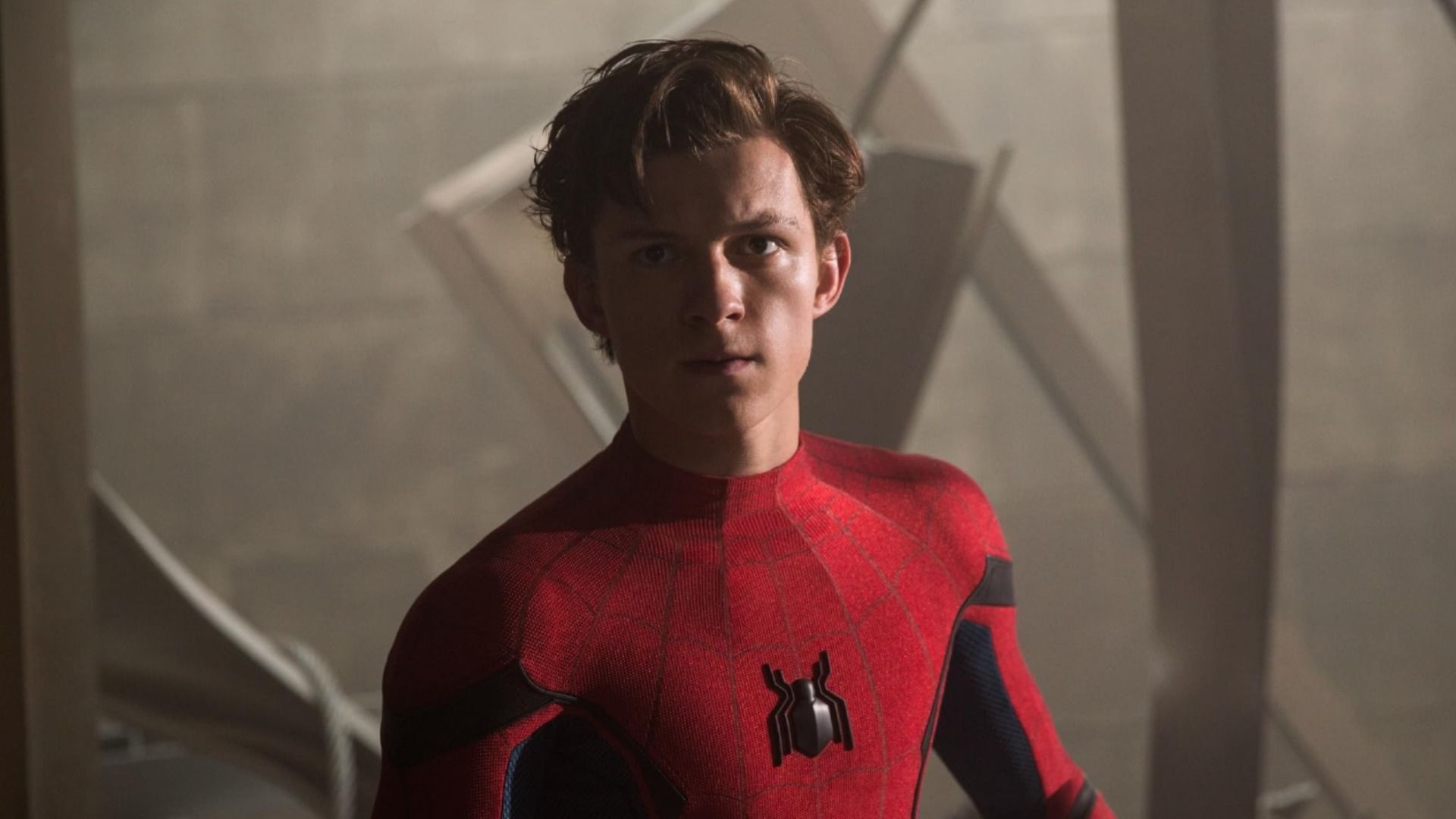 Aktor Tom Holland w czerwonym kostiumie superbohatera z emblematem pająka na piersi