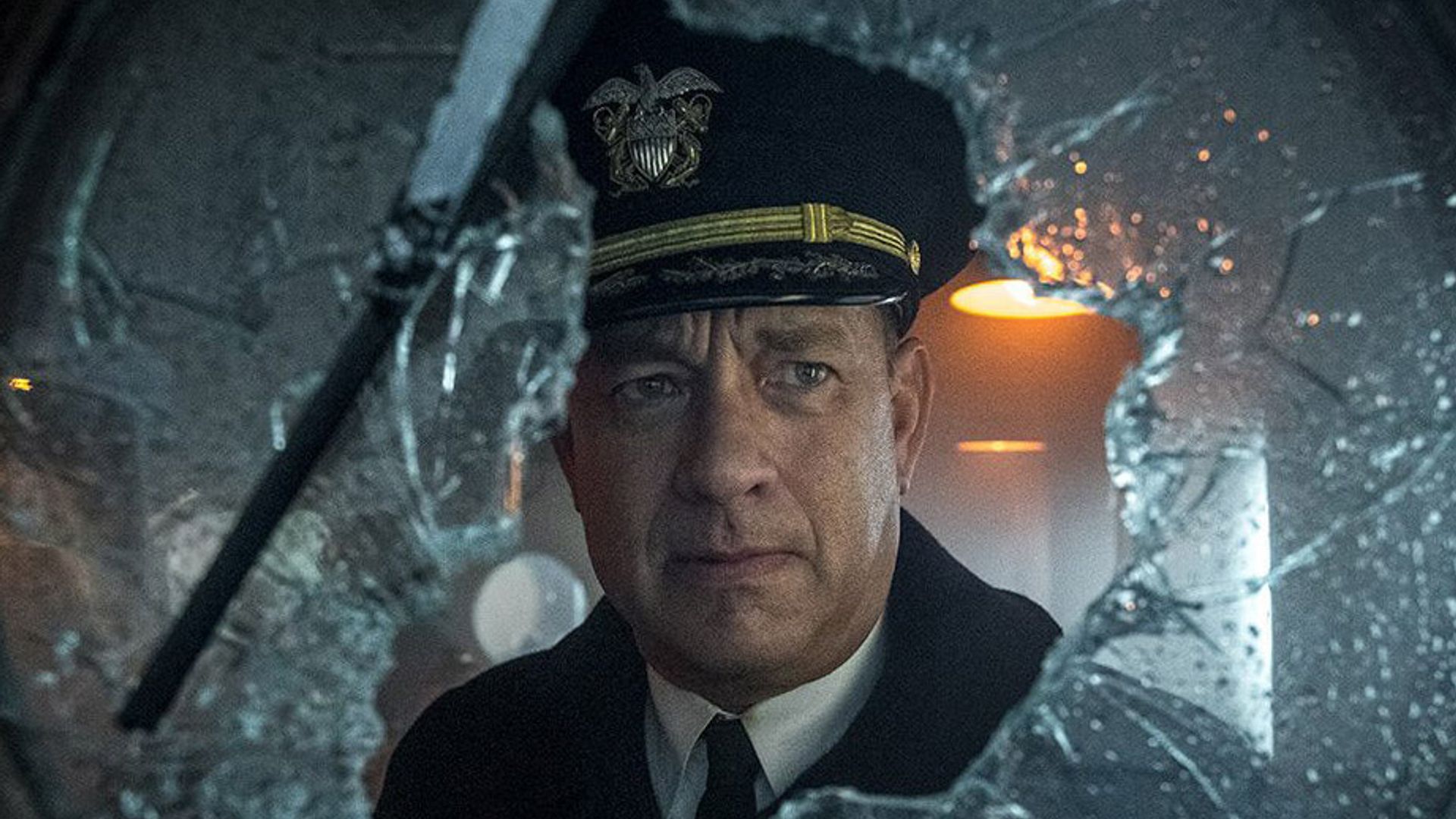 Tom Hanks w mundurze kapitana patrzy przez rozbite szkło z poważnym wyrazem twarzy