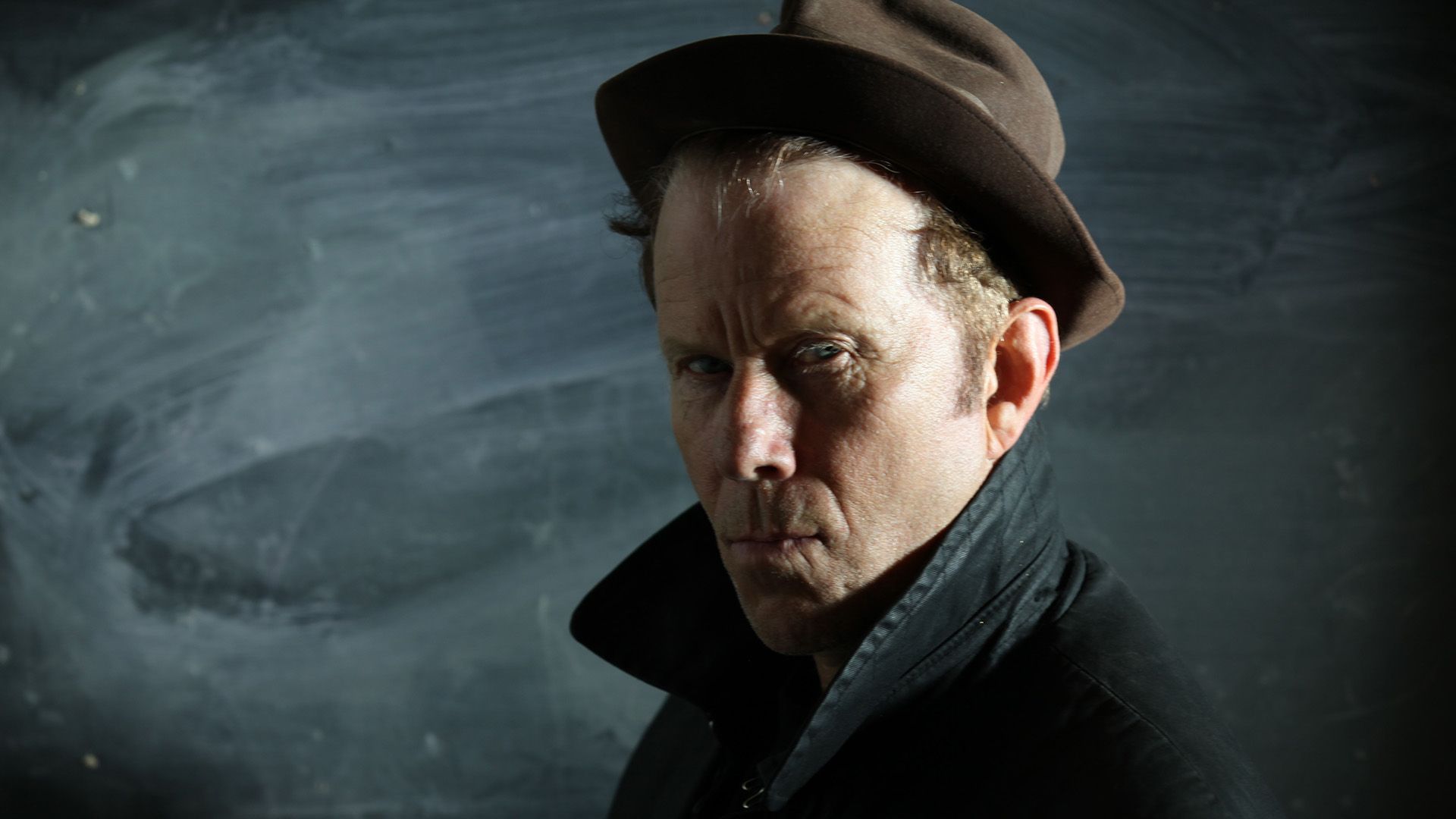 Muzyk Tom Waits w kapeluszu i płaszczu z podniesionym kołnierzem