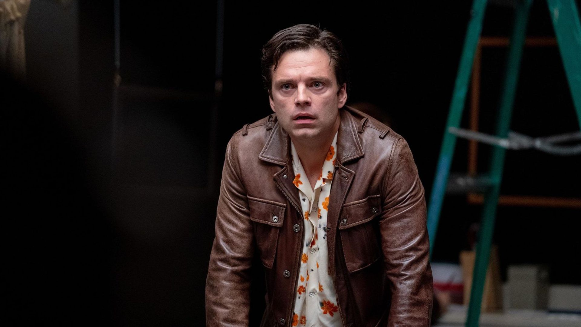 Sebastian Stan w brązowej kurtce patrzący przed siebie na czarnym tle