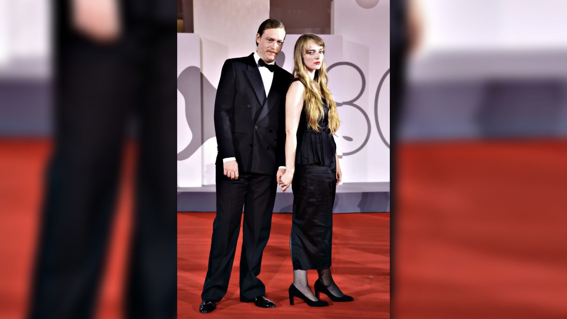Caleb Landry Jones i Katya Zverewa w wieczorowych strojach pozują na czerwonym dywanie, trzymając się za ręce