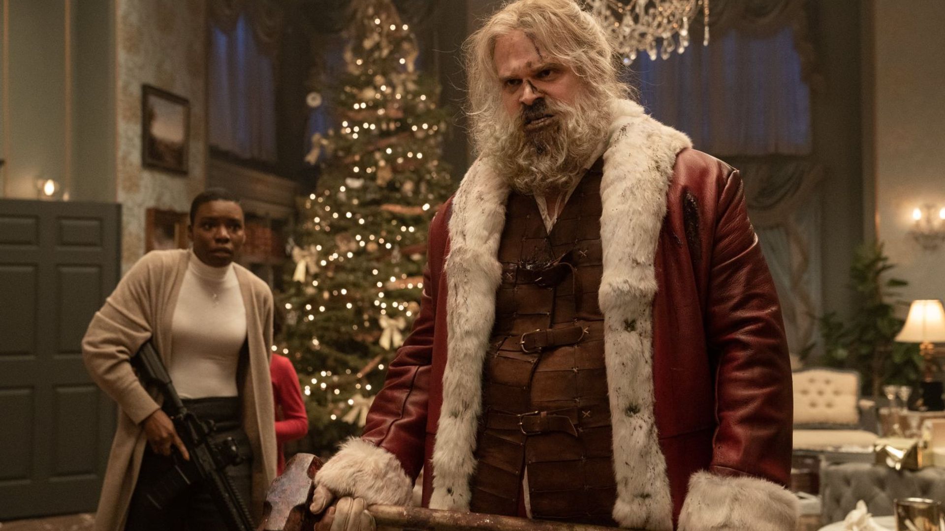 David Harbour w stroju Świętego Mikołaja trzymający siekierę, z świątecznym wnętrzem w tle
