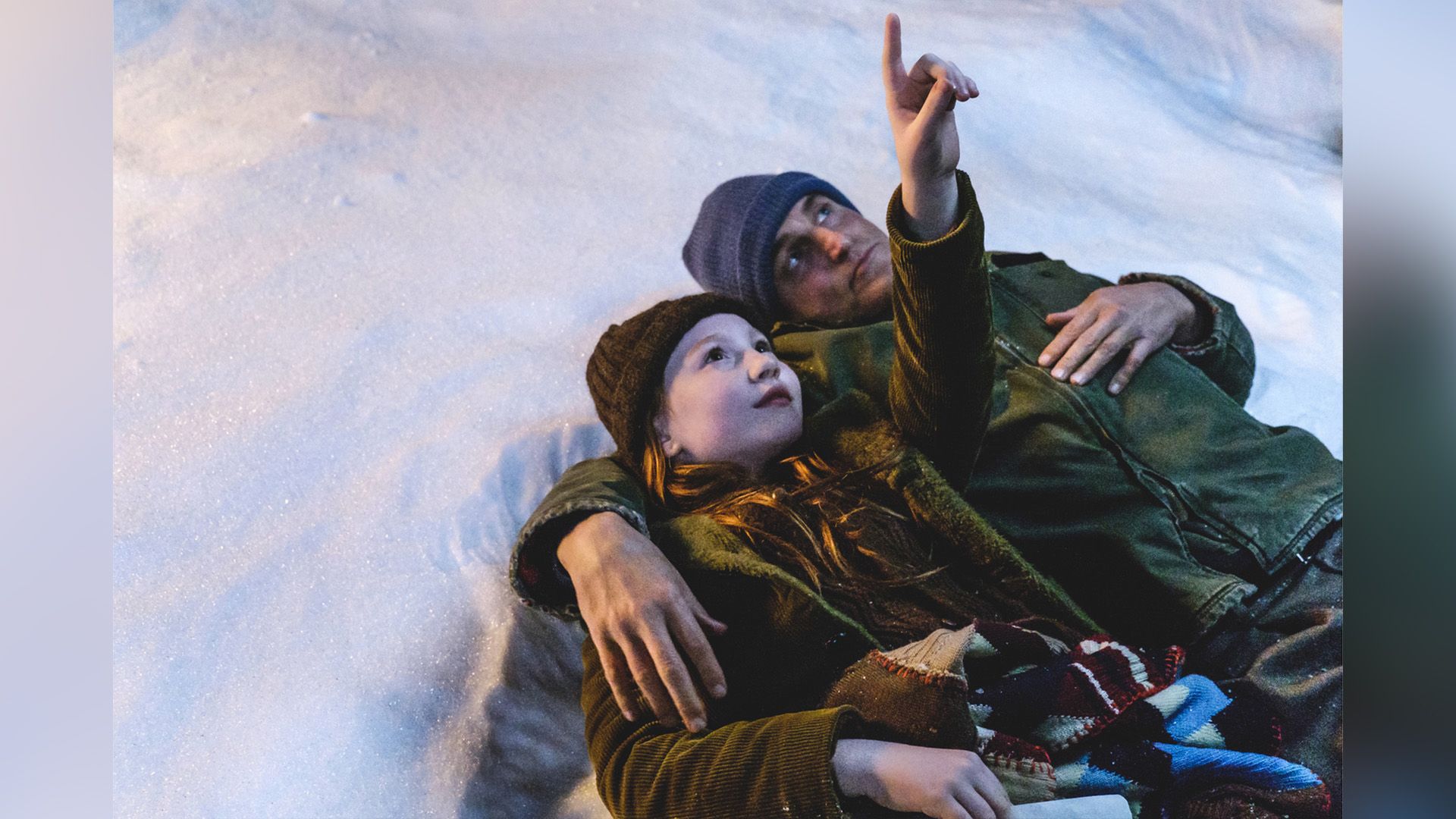 Ella Anderson i Woody Harrelson leżą na śniegu, a Ella wskazuje palcem w niebo