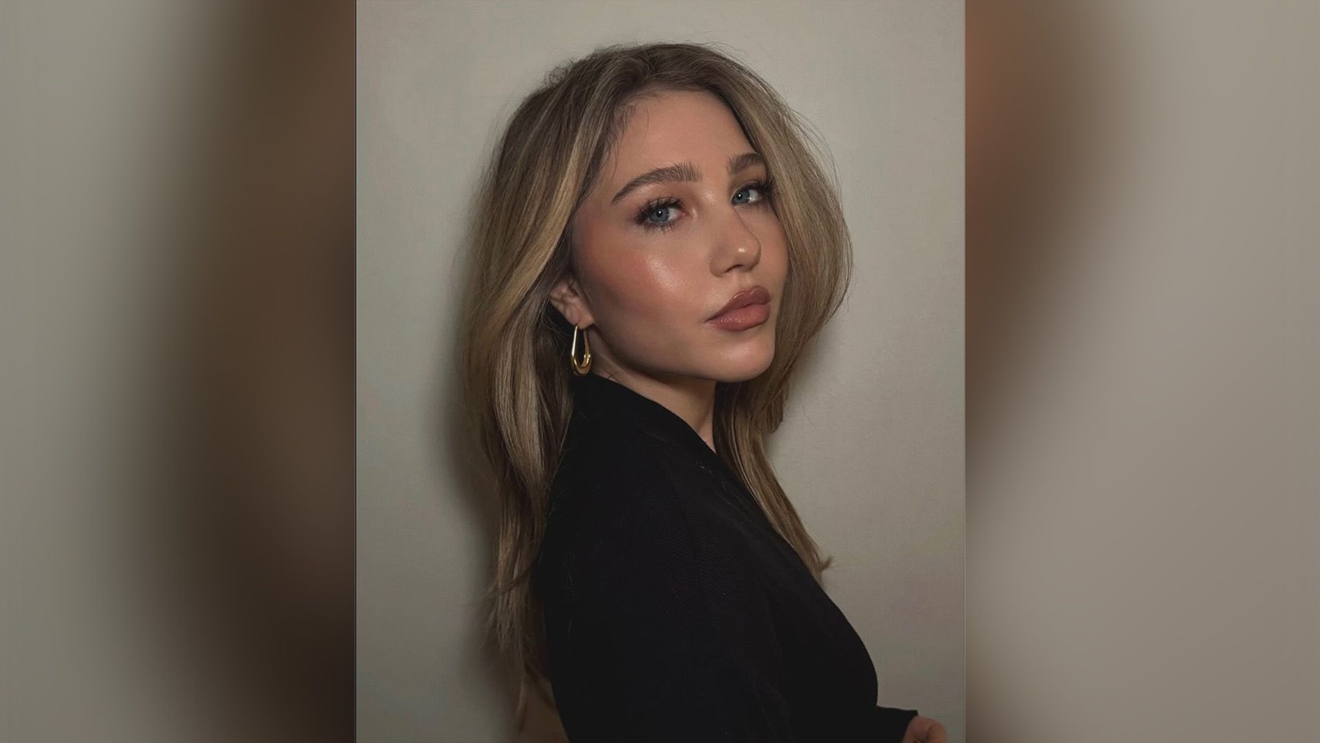 Ella Anderson w czarnej marynarce stojąca w pozycji trzy czwarte ze złotym kolczykiem