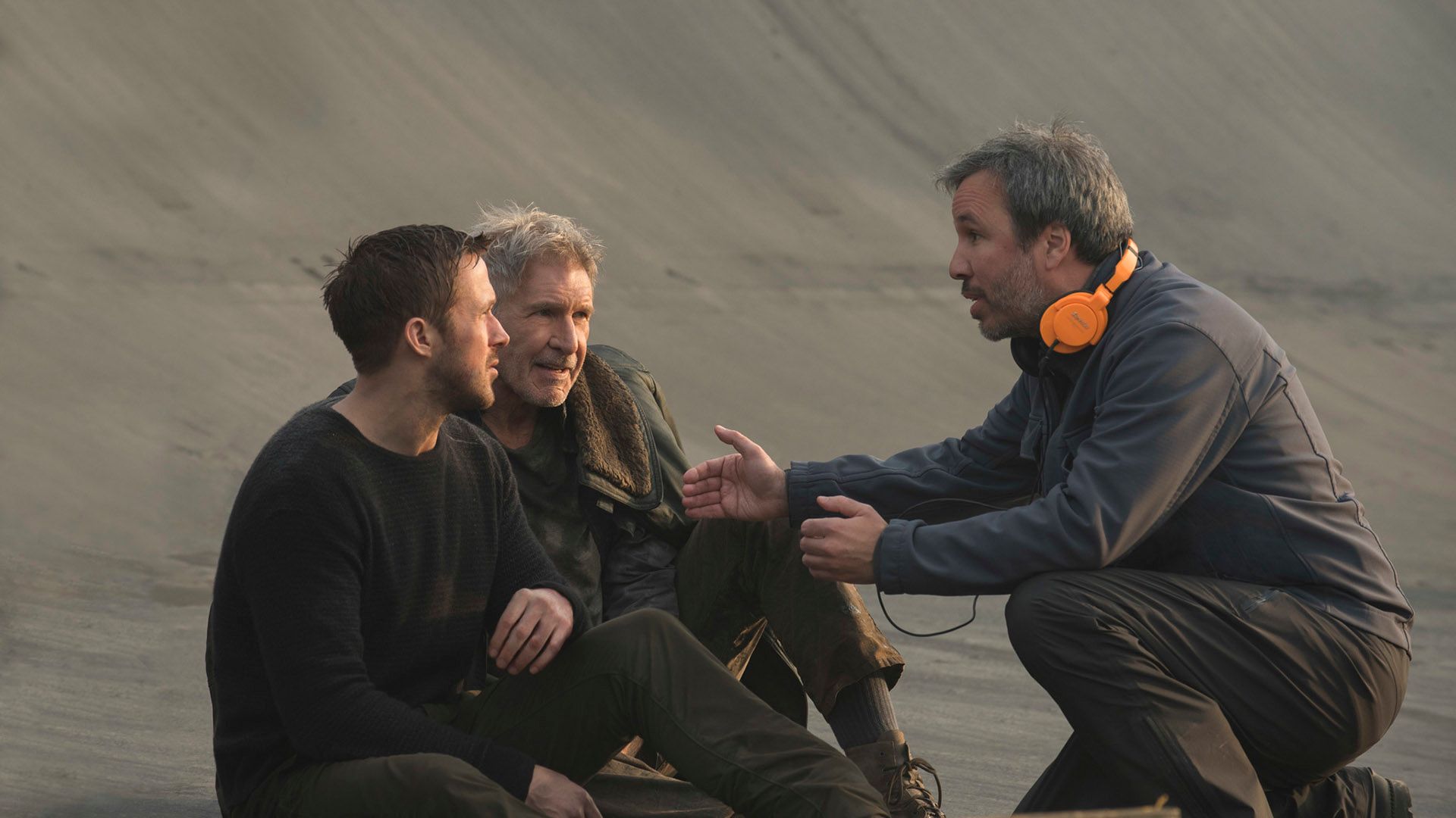 Denis Villeneuve gestykulujący, wyjaśnia coś Ryanowi Goslingowi i Harrisonowi Fordowi siedzącym przed nim