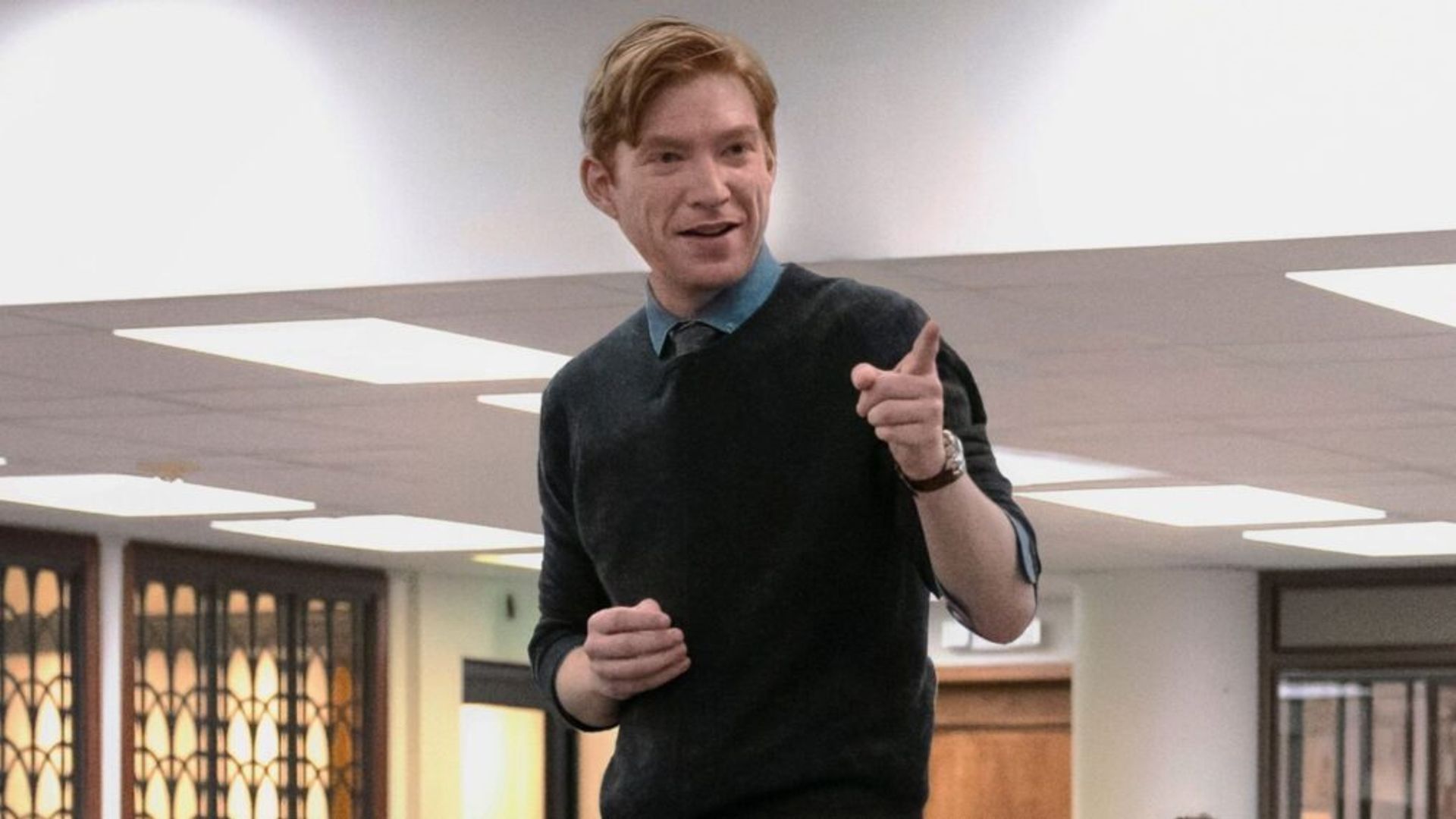 Domhnall Gleeson w granatowej bluzie stojący na stole i wskazujący palcem