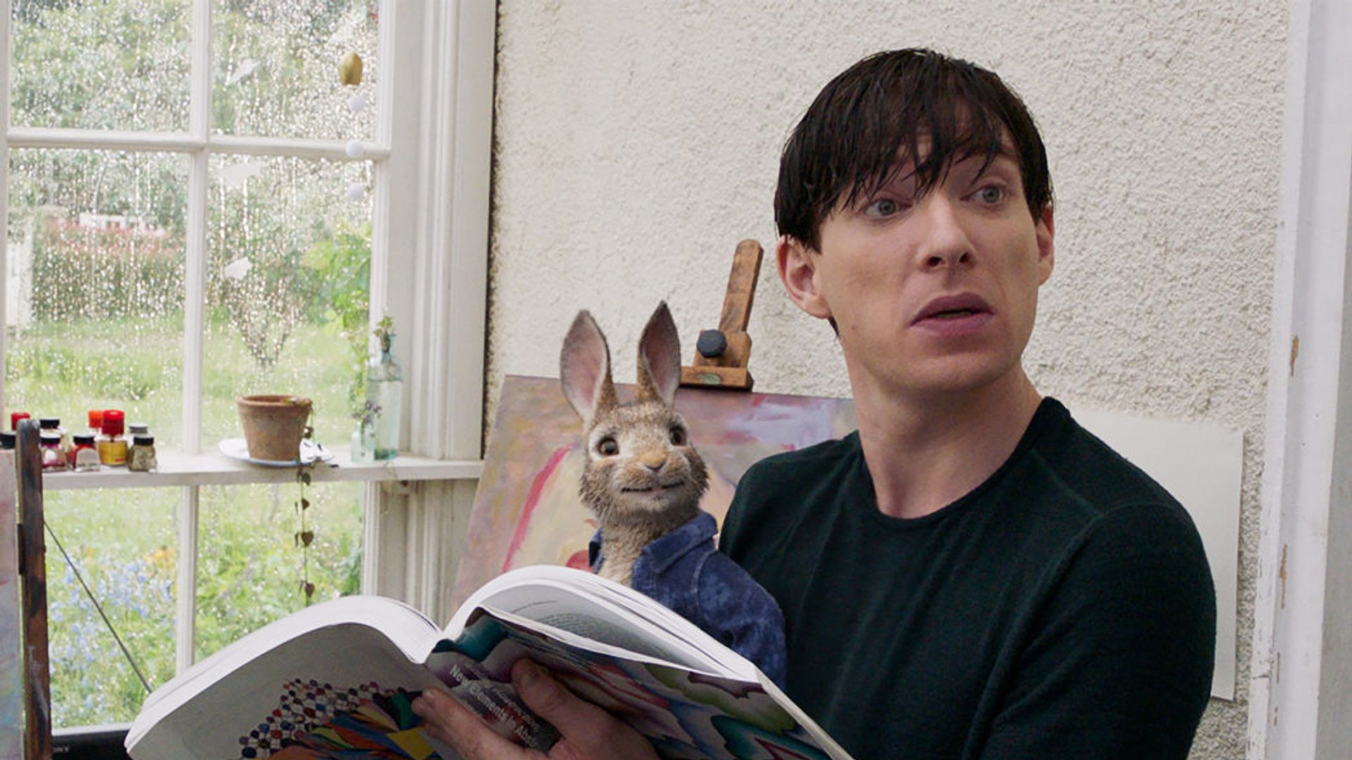 Domhnall Gleeson siedzi, czytając gazetę z zabawkowym królikiem na kolanach