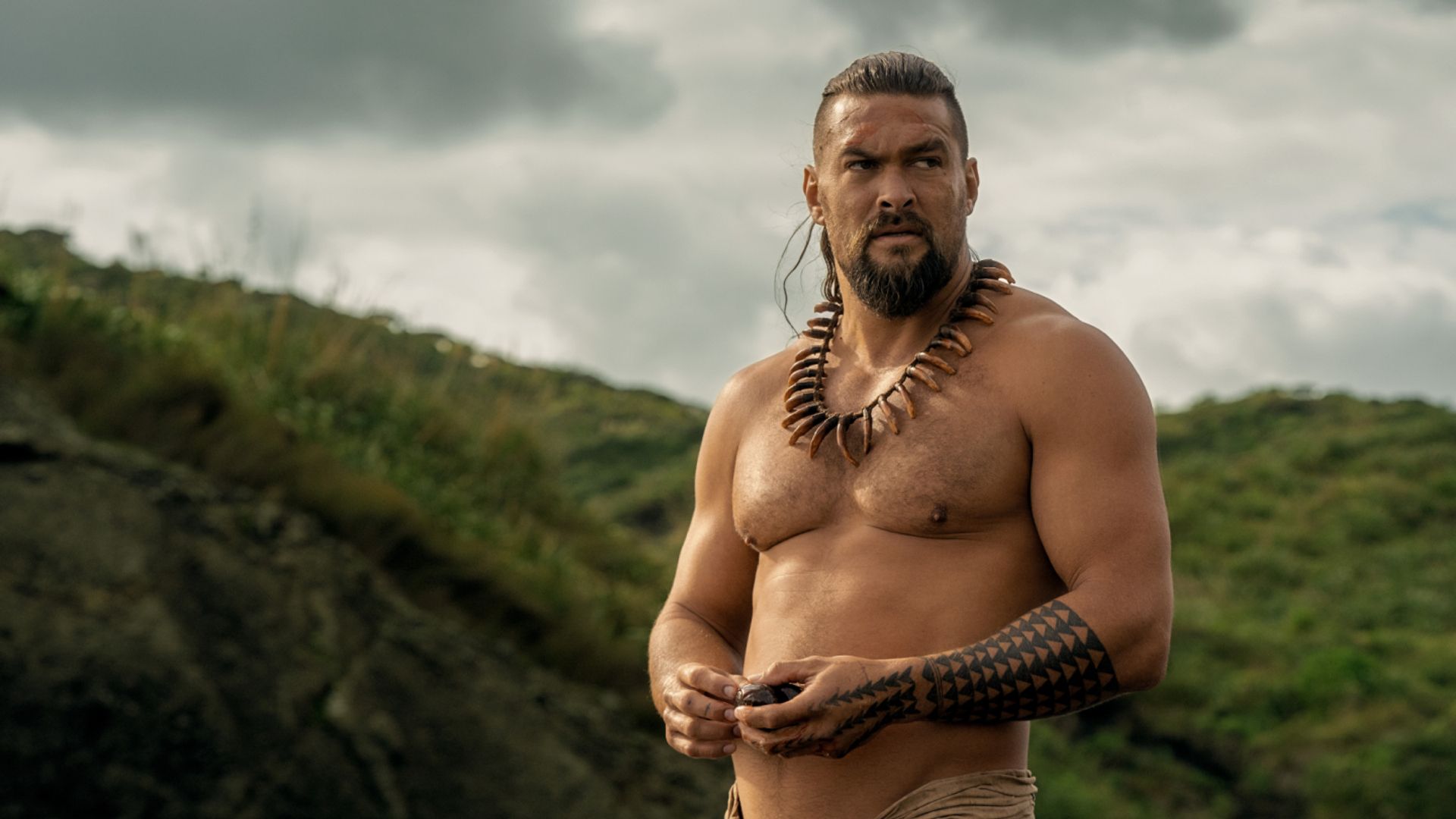 Jason Momoa bez koszuli z tradycyjnymi hawajskimi ozdobami i tatuażami na tle gór